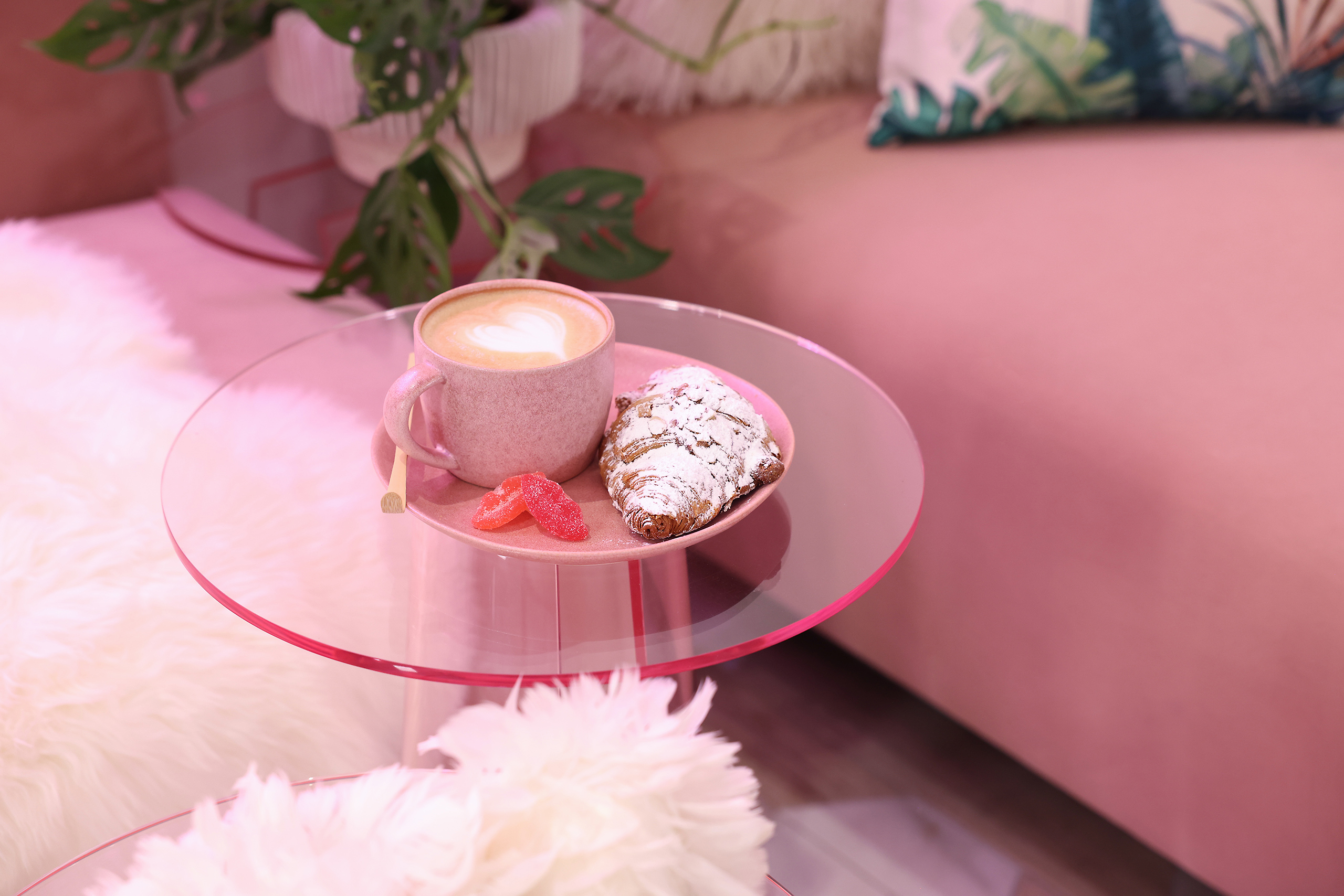 latte and a croissant setting on a small, pink, glass table