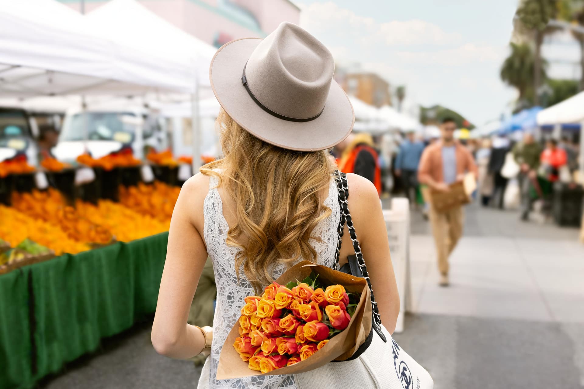 Woman shopping at outdoor farmers market with fresh flowers.