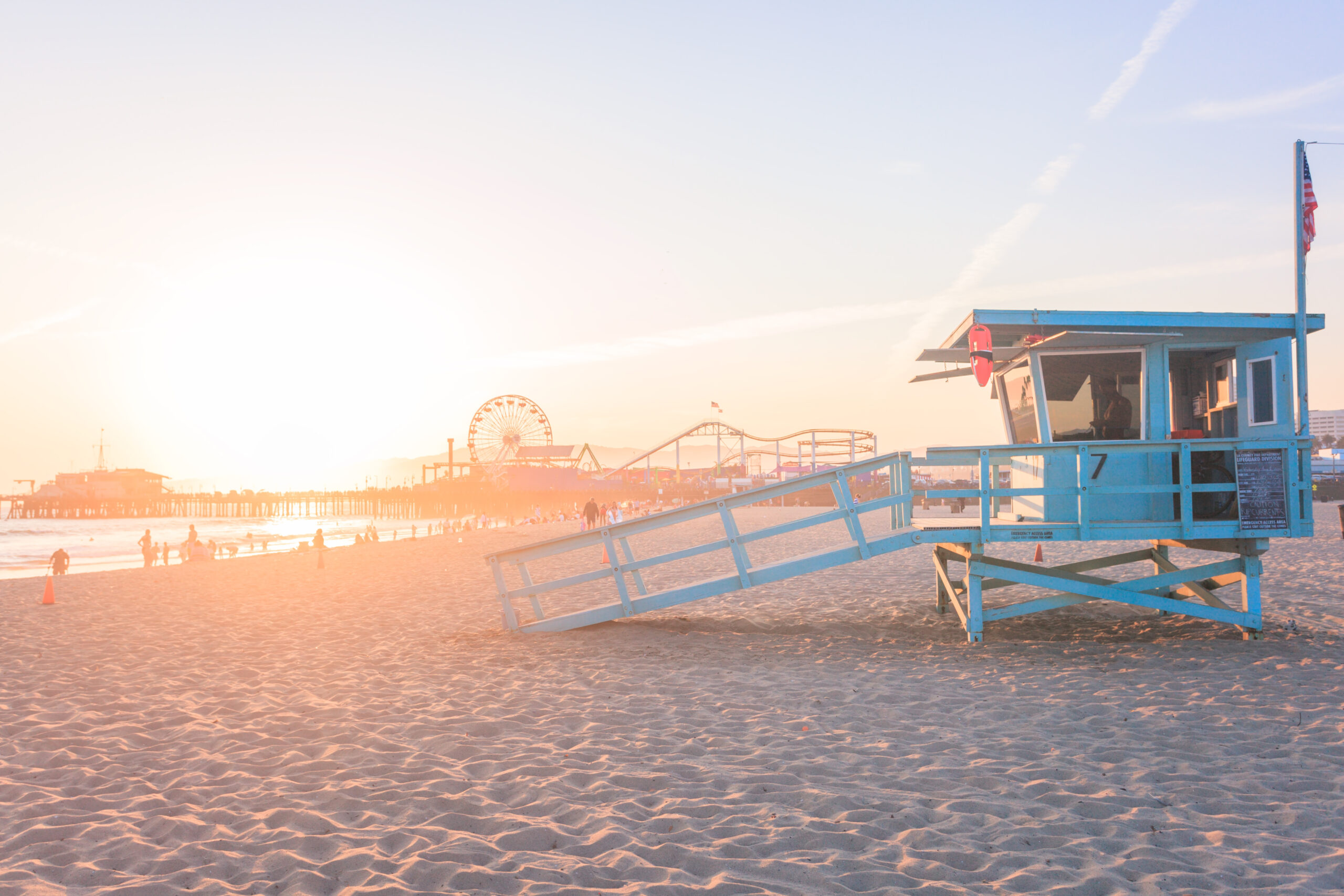 Lifeguard tower on a sandy beach at sunset with a pier and Ferris wheel in the background.