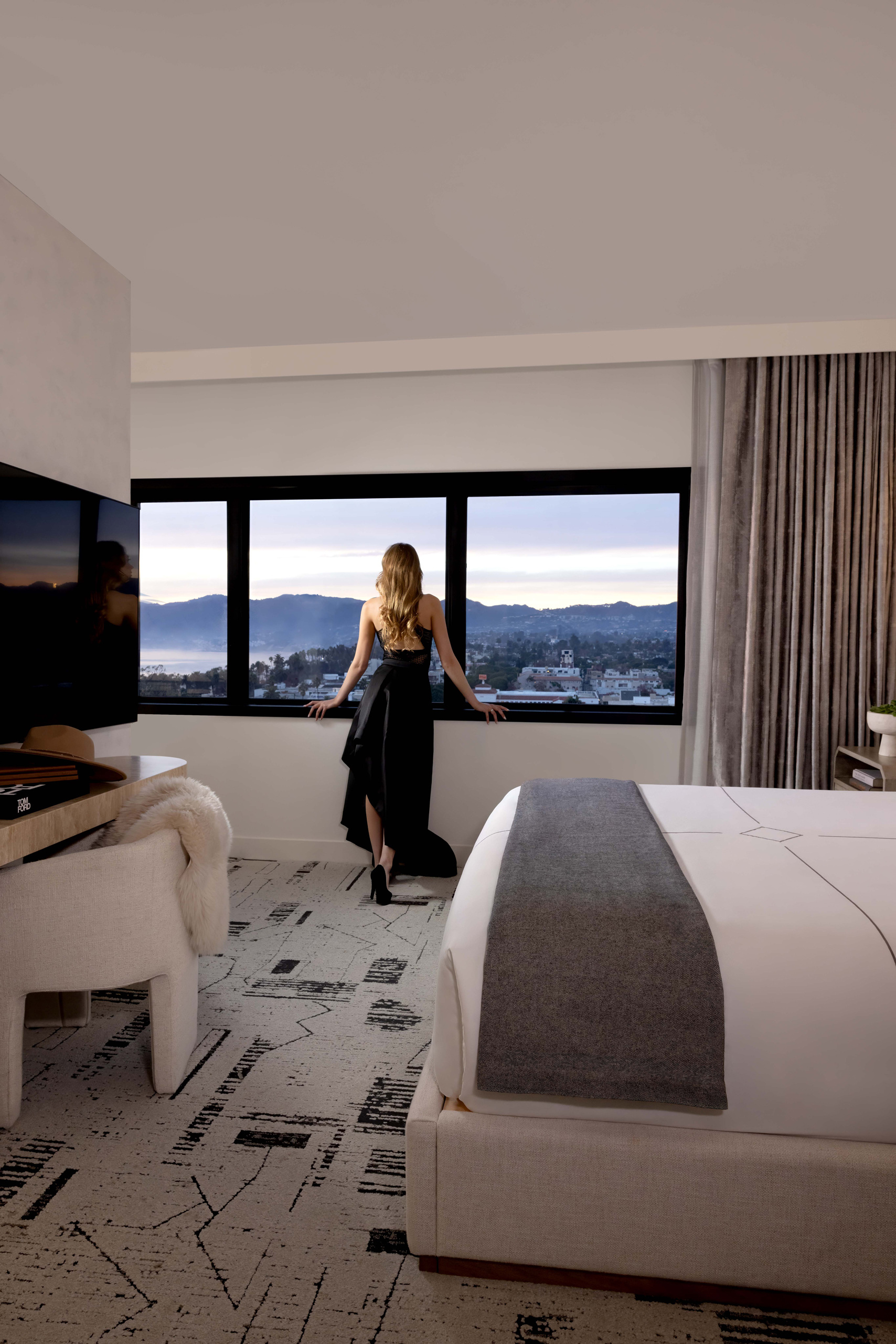 Woman in elegant dress looking out hotel room window.