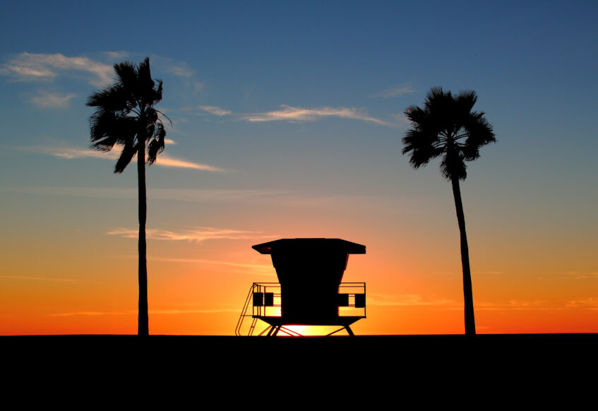 Lifeguard tower and palm trees silhouetted at sunset.