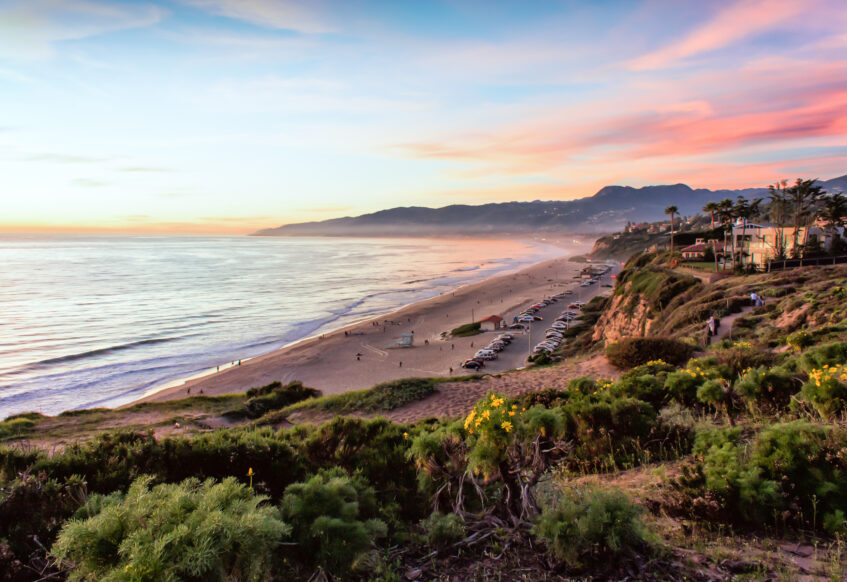 Scenic coastline view at sunset with beach and cliffs.