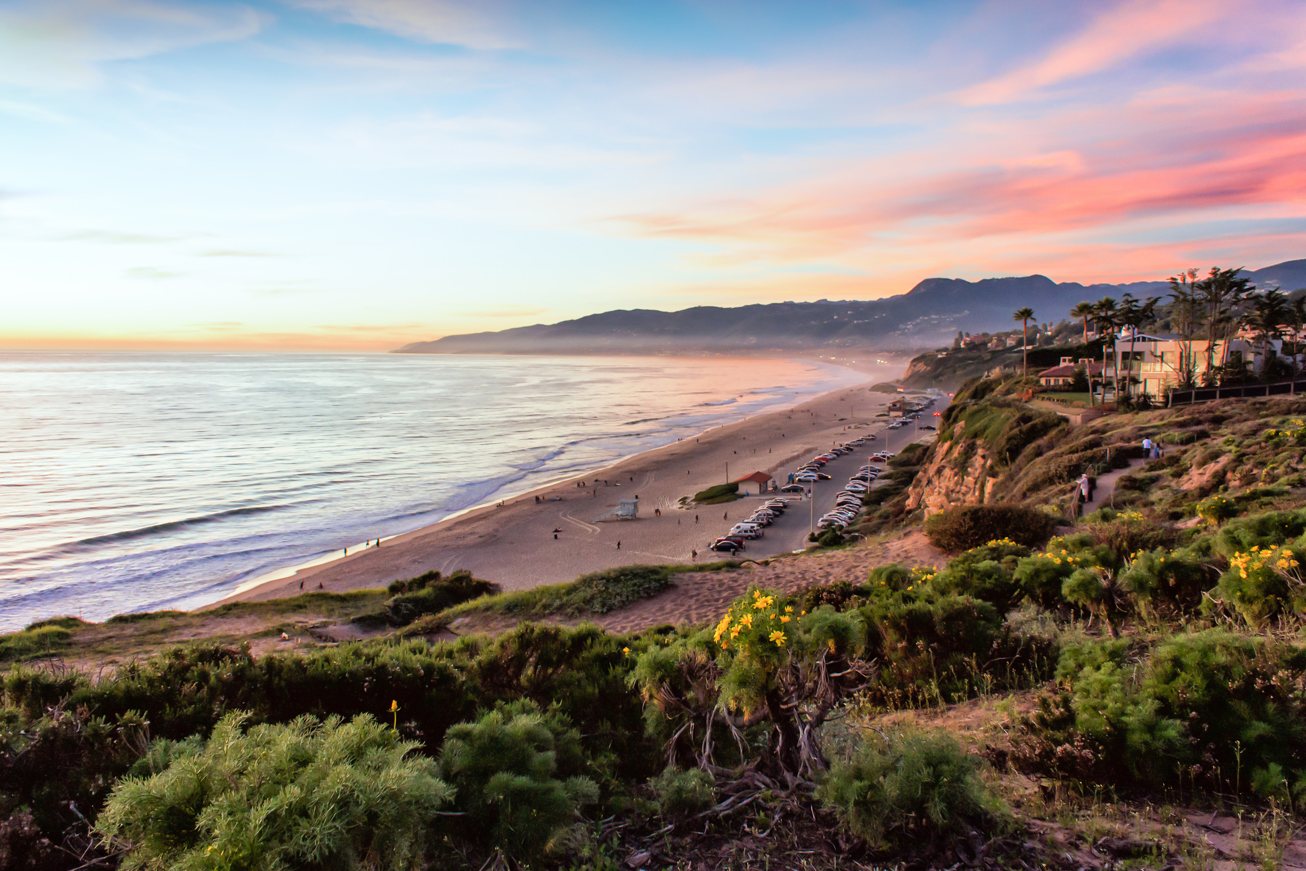 Scenic coastline view at sunset with beach and cliffs.