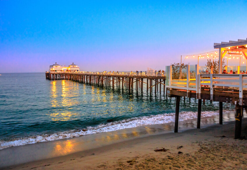 Malibu Pier at sunset with glowing lights over the ocean.
