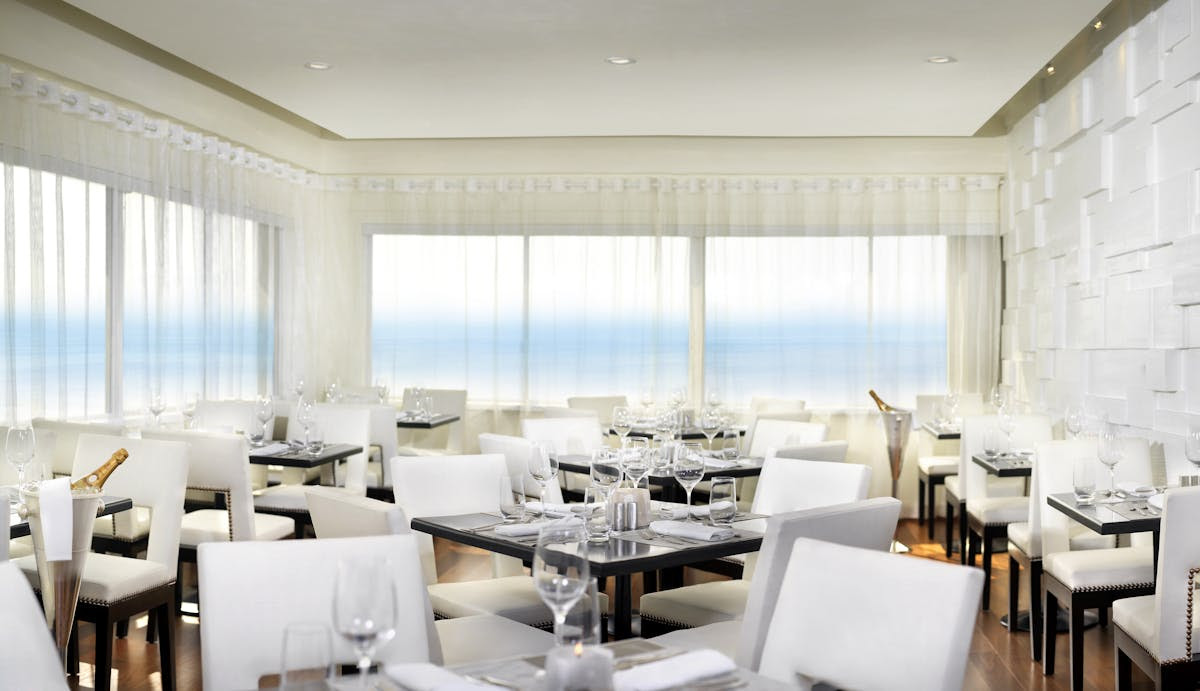 Elegant oceanfront dining room with white chairs and sheer curtains