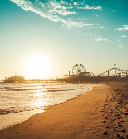 Sunset over sandy beach with waves and pier featuring Ferris wheel