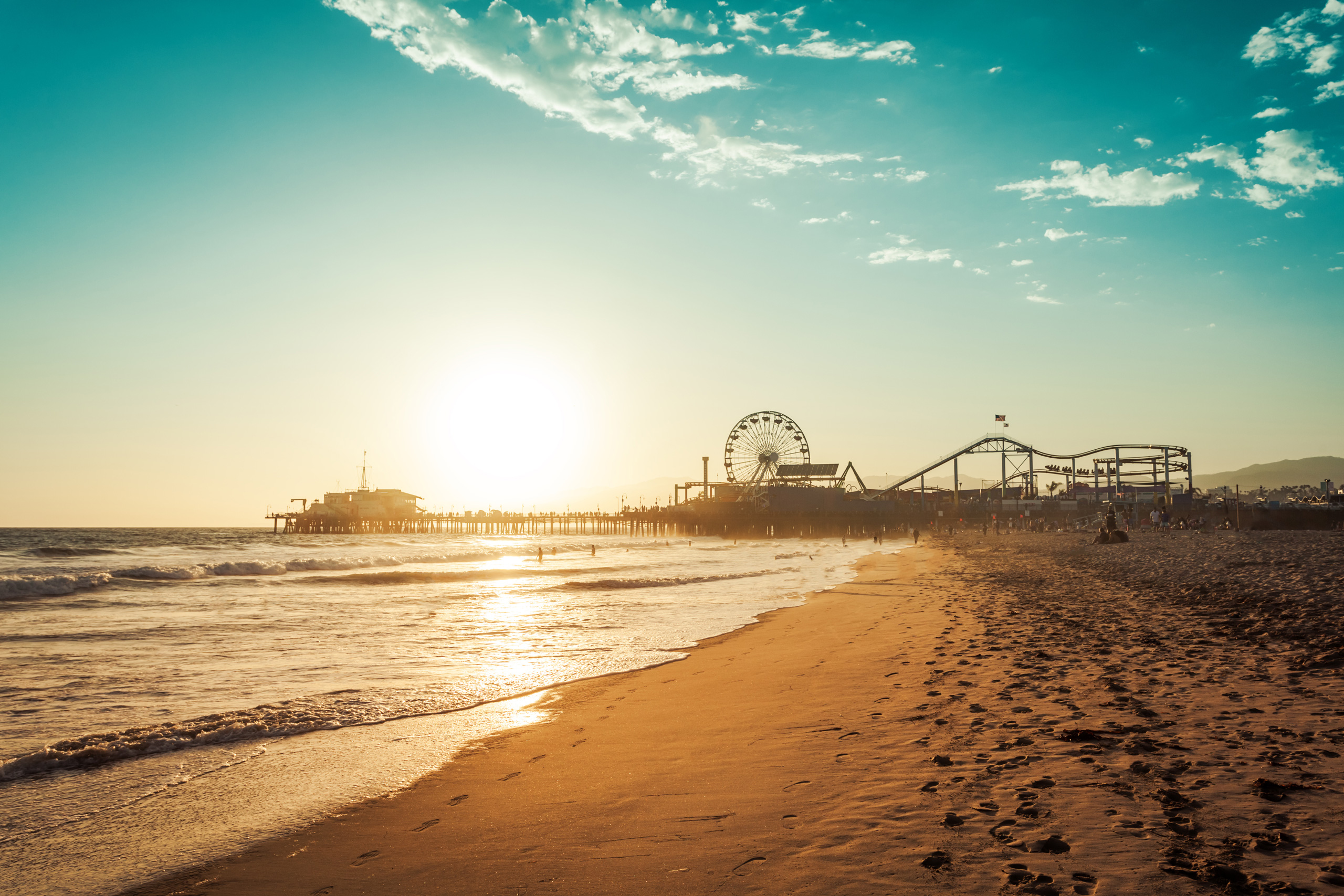 Sunset over sandy beach with waves and pier featuring Ferris wheel