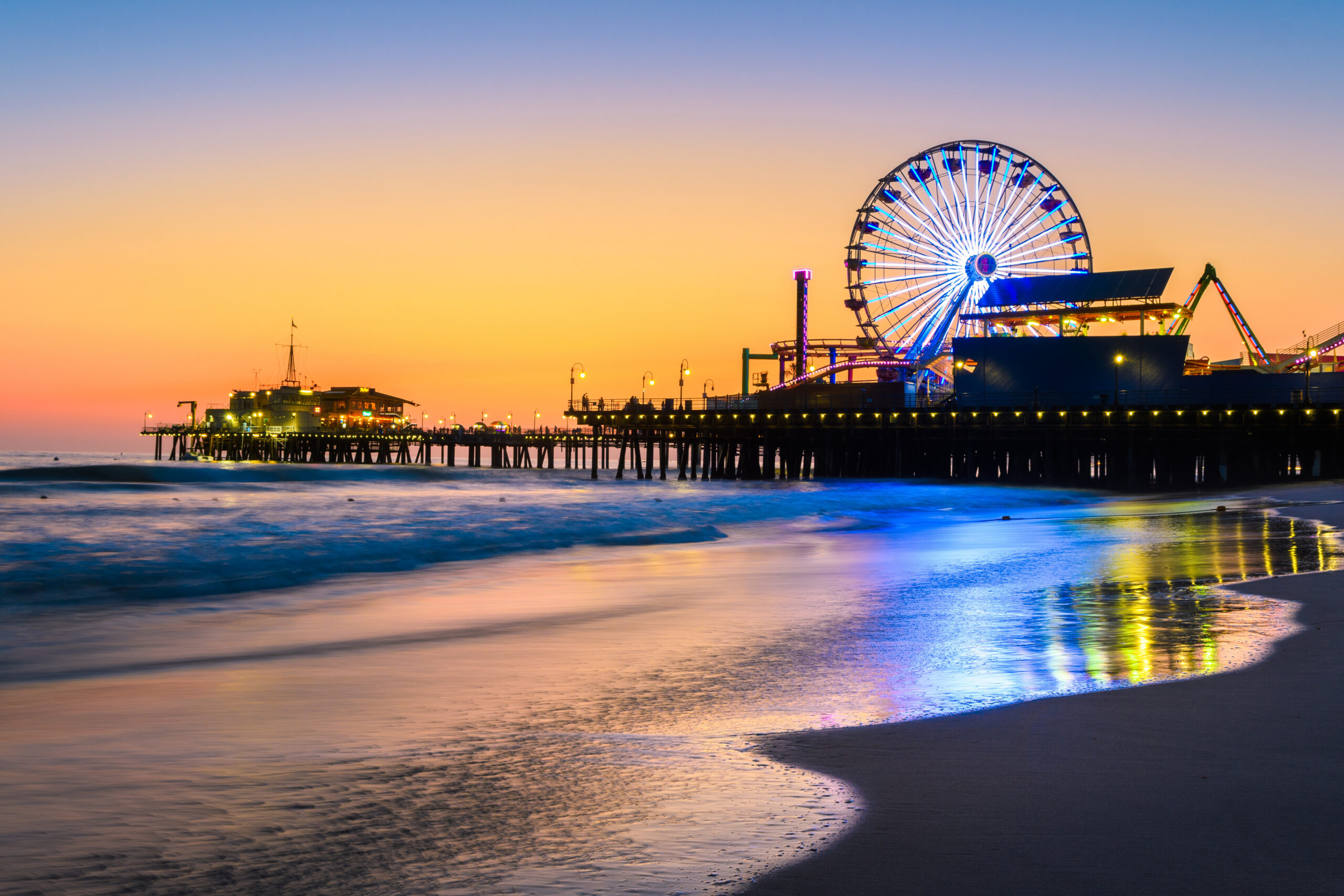 Santa Monica Pier at sunset with Ferris wheel glowing over the shoreline