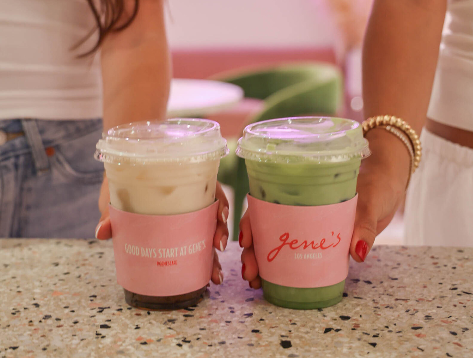 Close-up of two iced drinks—matcha and latte—in pink “Jene’s Los Angeles” cups on a counter