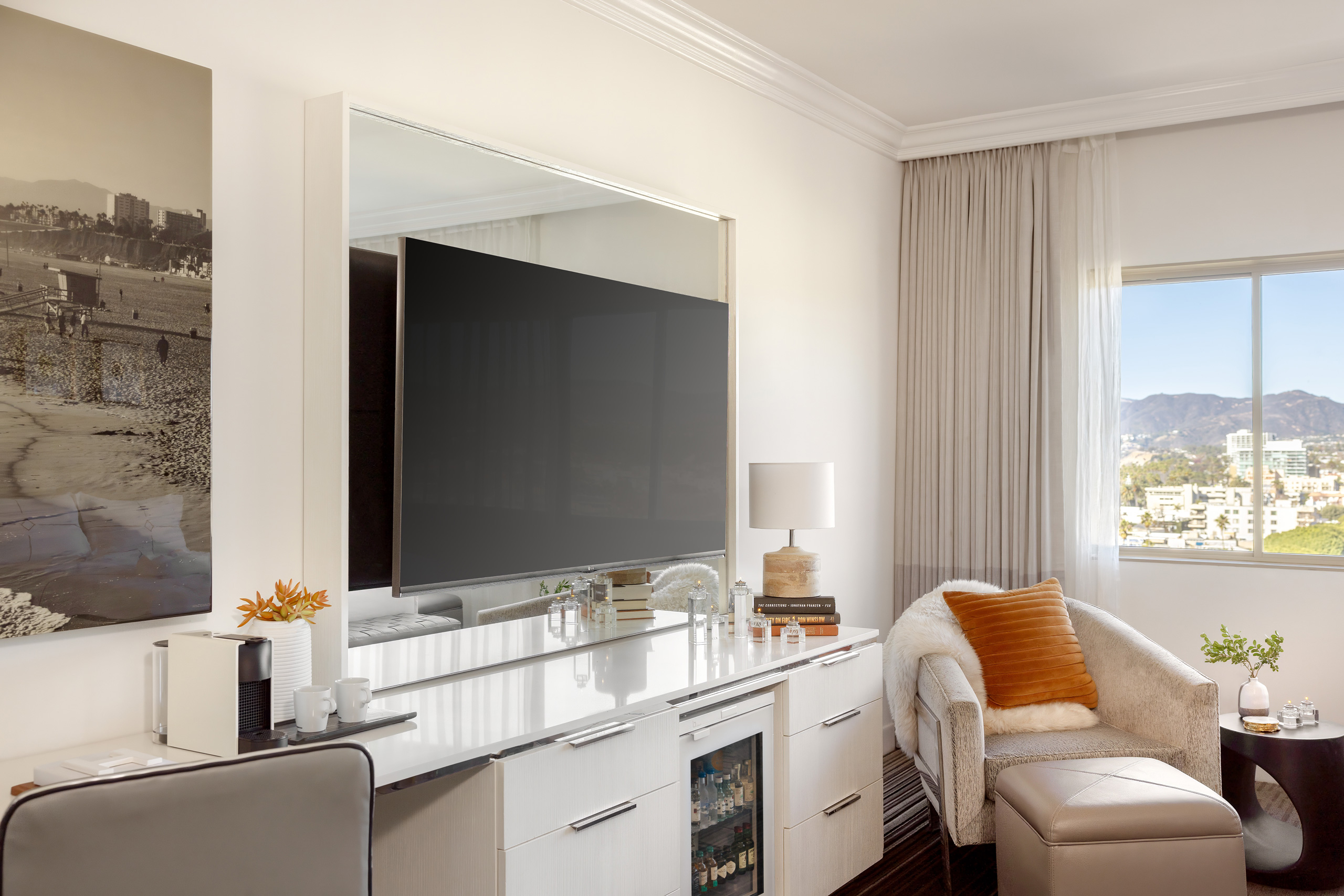 Neutral-toned interior with a large TV, built-in cabinet, and city view through sheer curtains