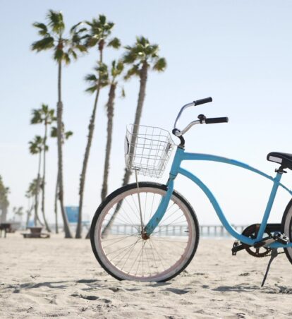 a baby blue beach cruiser resting in the sand with palm trees in the distance