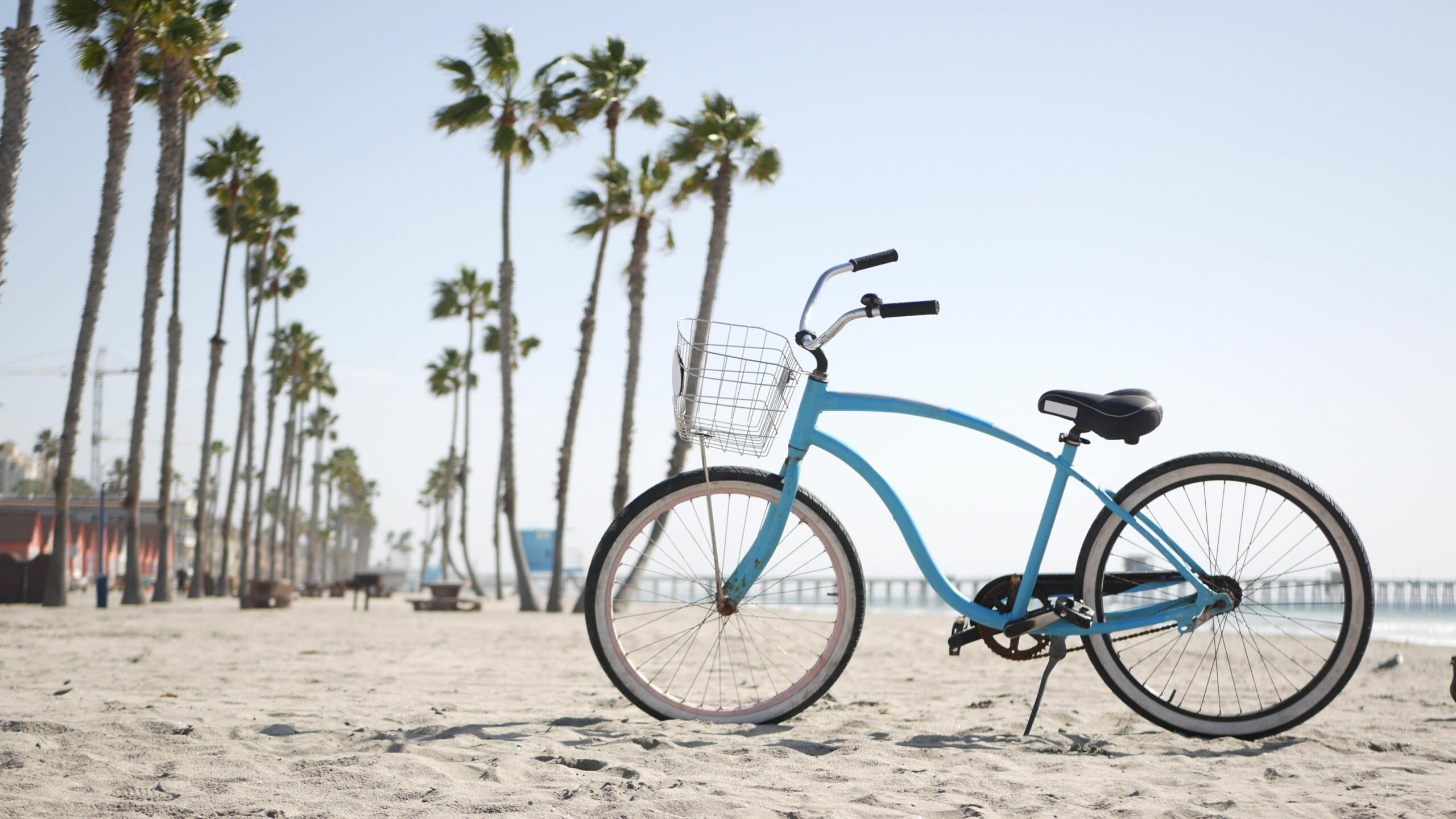 a baby blue beach cruiser resting in the sand with palm trees in the distance