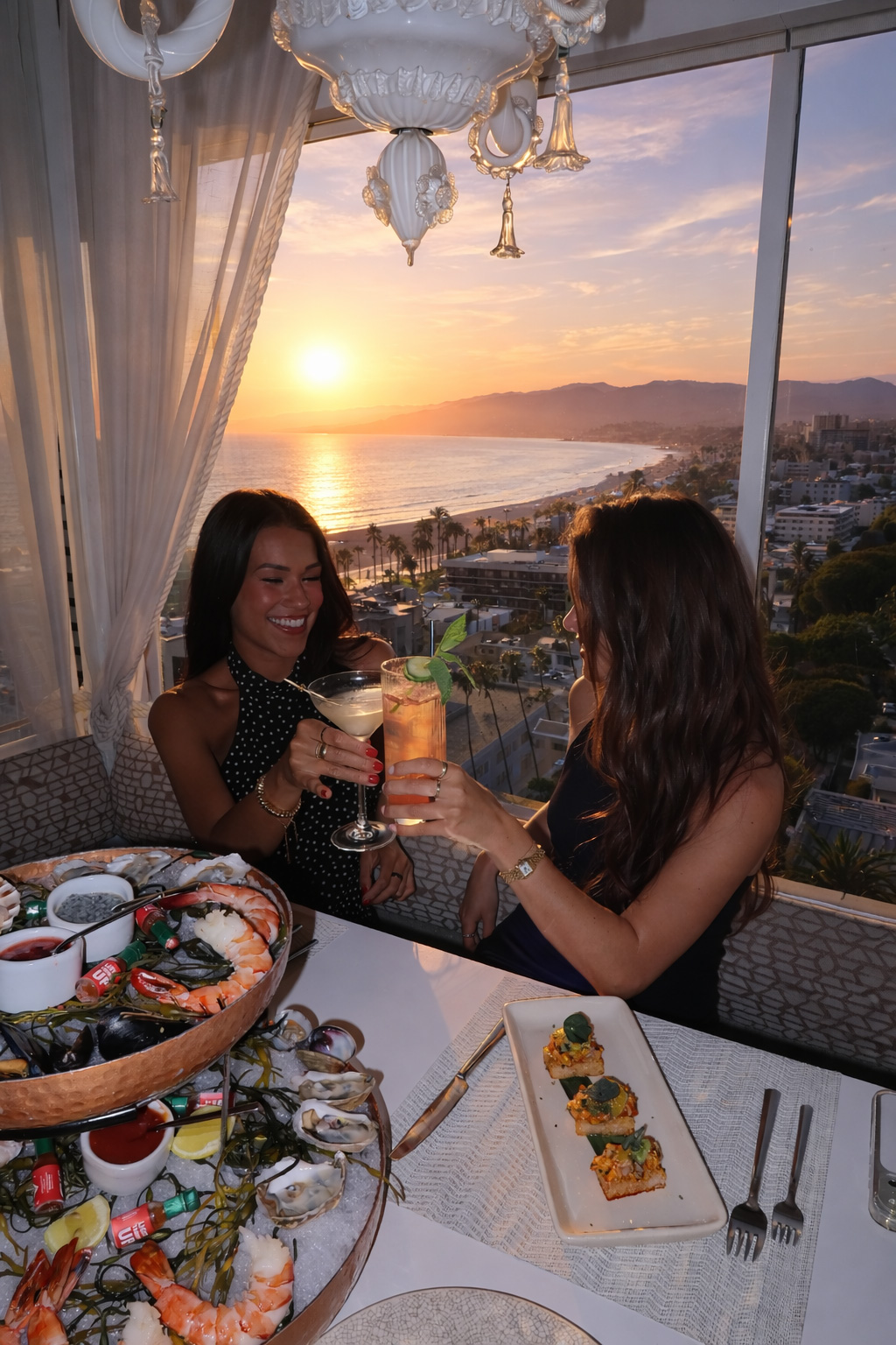 Two women toasting cocktails at a seaside restaurant during sunset with ocean views