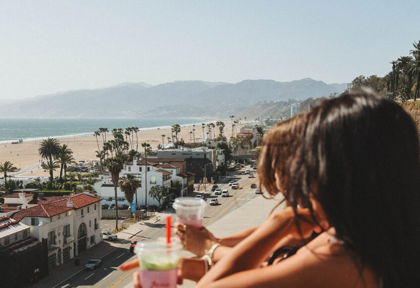 Two people enjoying drinks while overlooking a coastal city and beach view.