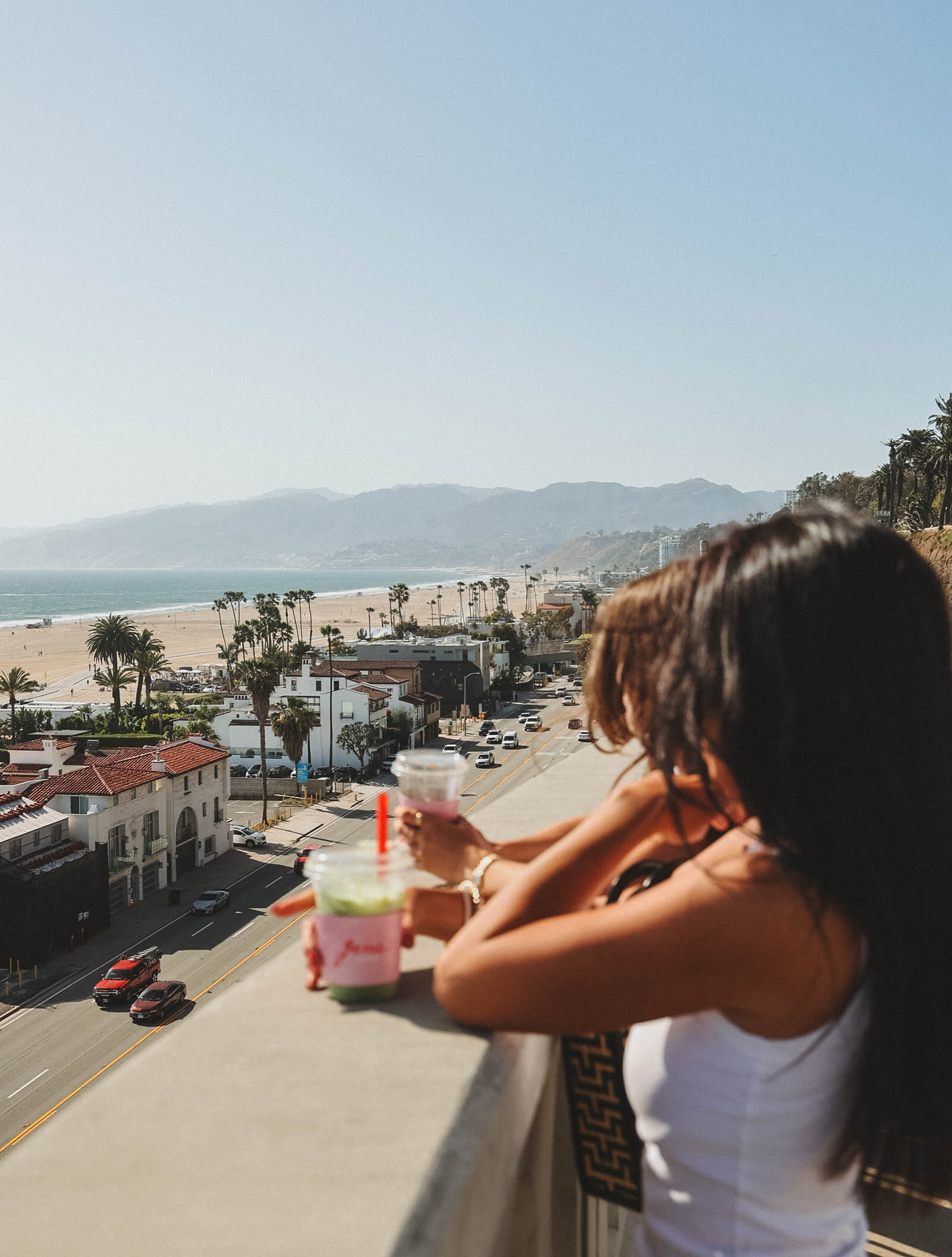 Two people enjoying drinks while overlooking a coastal city and beach view.