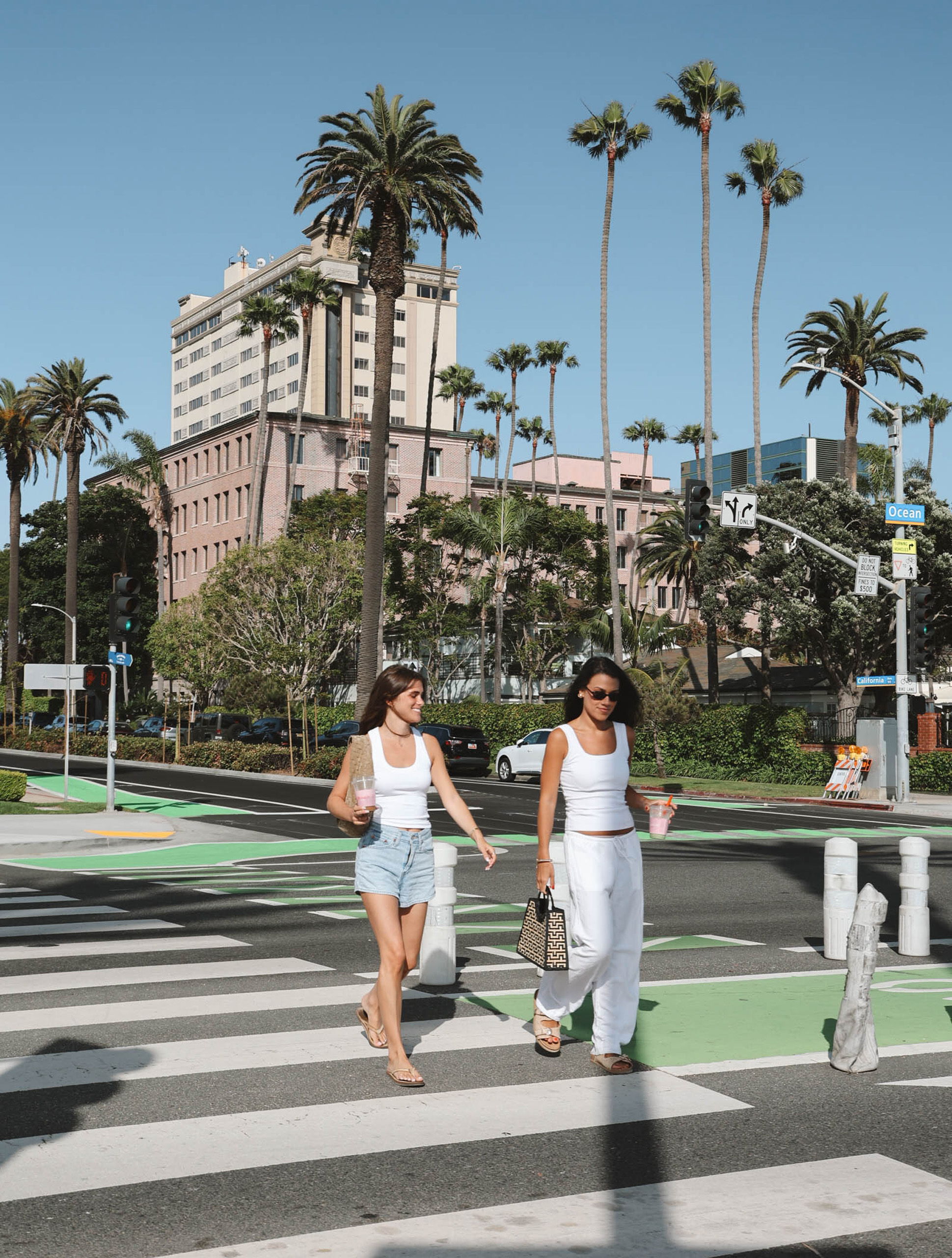 Two people crossing a palm-lined city street near the beach.