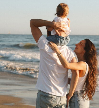 Family walking along the beach with a child on an adult’s shoulders.