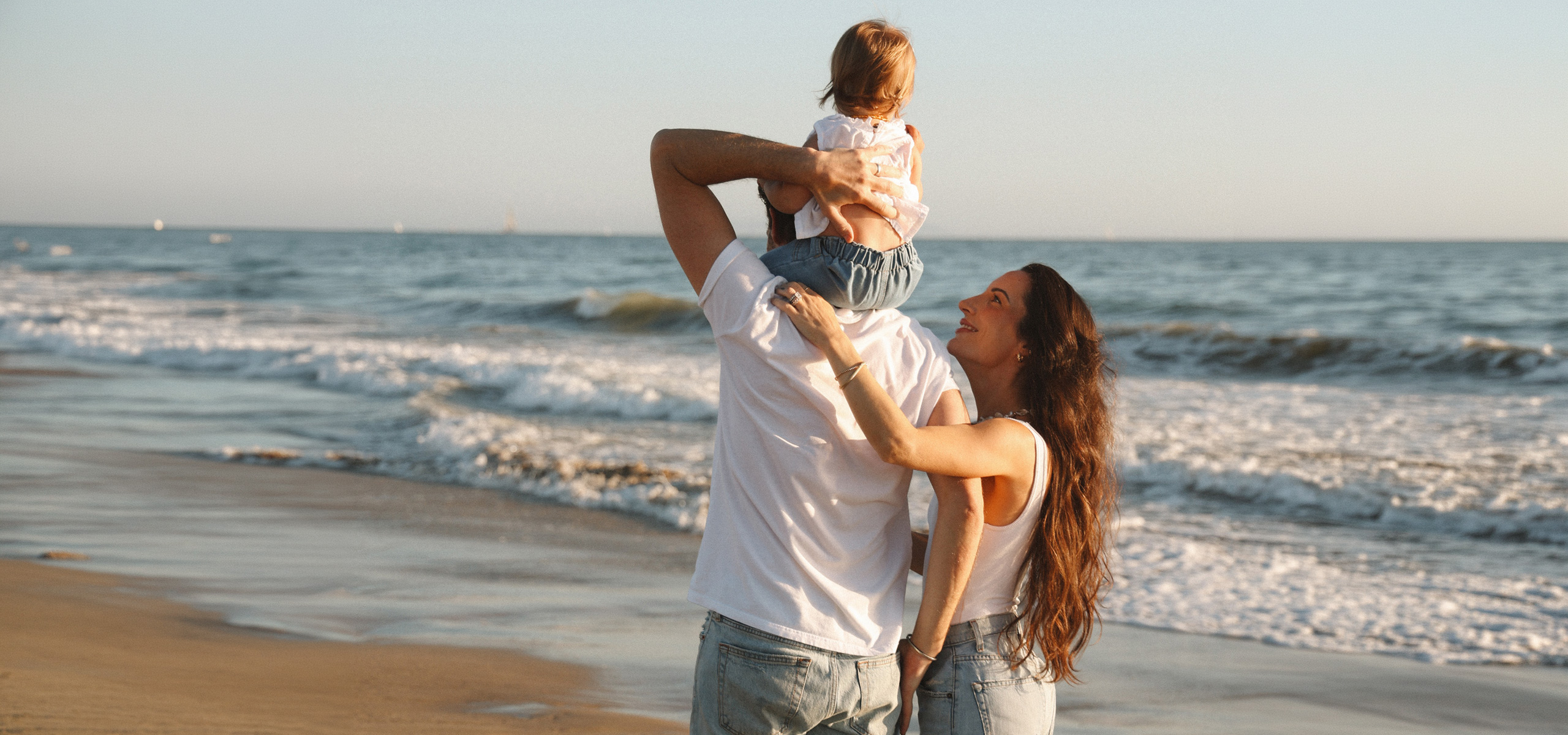 Family walking along the beach with a child on an adult’s shoulders.